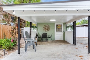 A covered patio area with a table and chairs, a decorative wall, and a door with a sign. - Cozy 2-bedroom house in charming Tampa with AC (Tampa)
