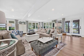 A spacious living room with a large window, a sofa set, a coffee table, and a glass-top table. - Winyah Bay A Luxury Waterfront Estate with Guest House and Pool (Georgetown)