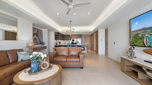 Ein modernes Wohnzimmer mit einem braunen Ledersofa, einem runden Couchtisch und einem Flachbildfernseher auf einem Holzständer.