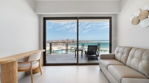 Ein modernes Wohnzimmer mit einer Couch, einem Holztisch und Stühlen, mit Blick auf einen Strand und Poolbereich.