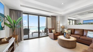 A spacious living room with a large window offering a view of the beach, a brown leather sofa, a coffee table, and a dining area with a view. - Two 501: Beachfront Paradise | Sonoran Star Resort (Puerto Peñasco)