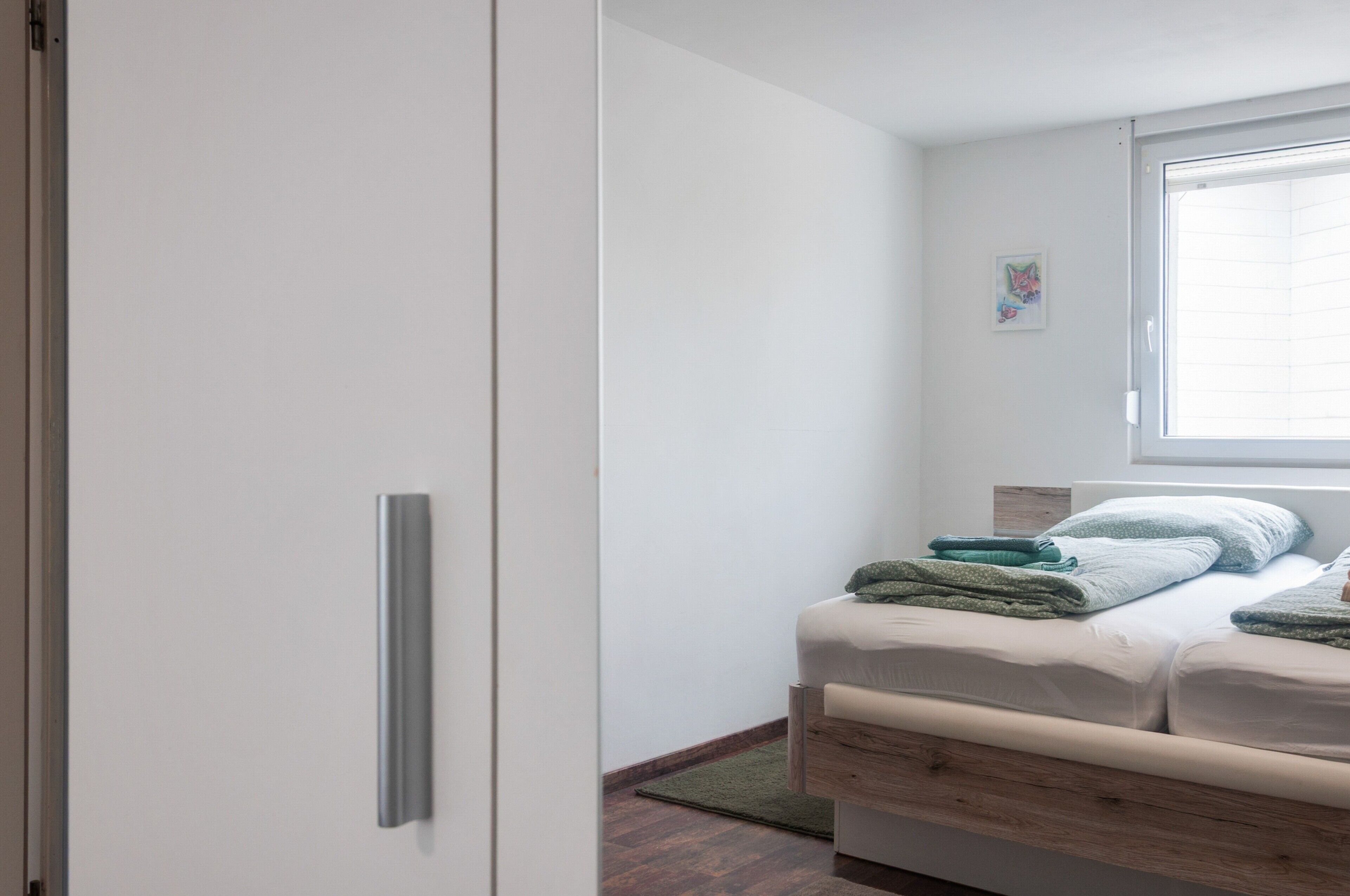 Ein Schlafzimmer mit einem Bett, einem Kleiderschrank, einem Fenster und einem kleinen Kunstwerk an der Wand.