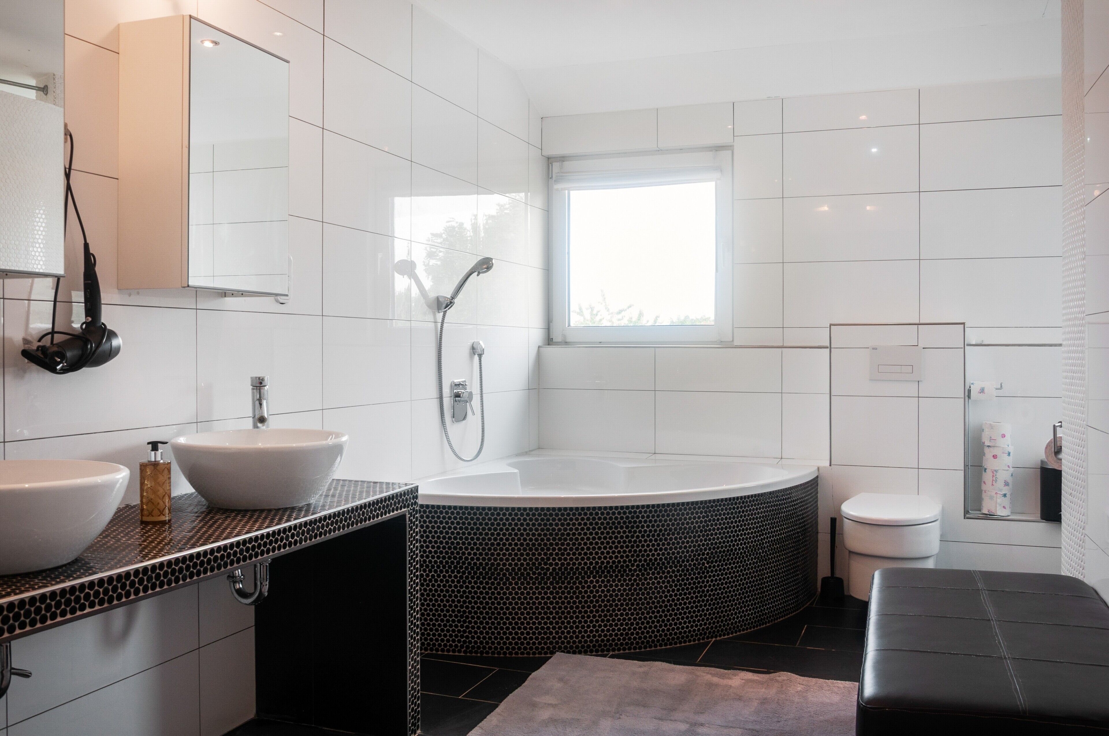 Ein modernes Badezimmer mit einer großen Badewanne, einem Doppelwaschtisch, einer Toilette und einem Fenster für natürliches Licht.