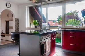 A modern kitchen with a central island, red cabinets, and a view of the neighborhood through large windows.