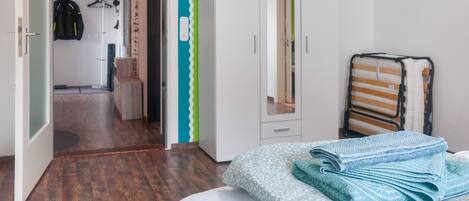 A bedroom with a wardrobe, a bed with a blue and white patterned bedspread, and a mirror.