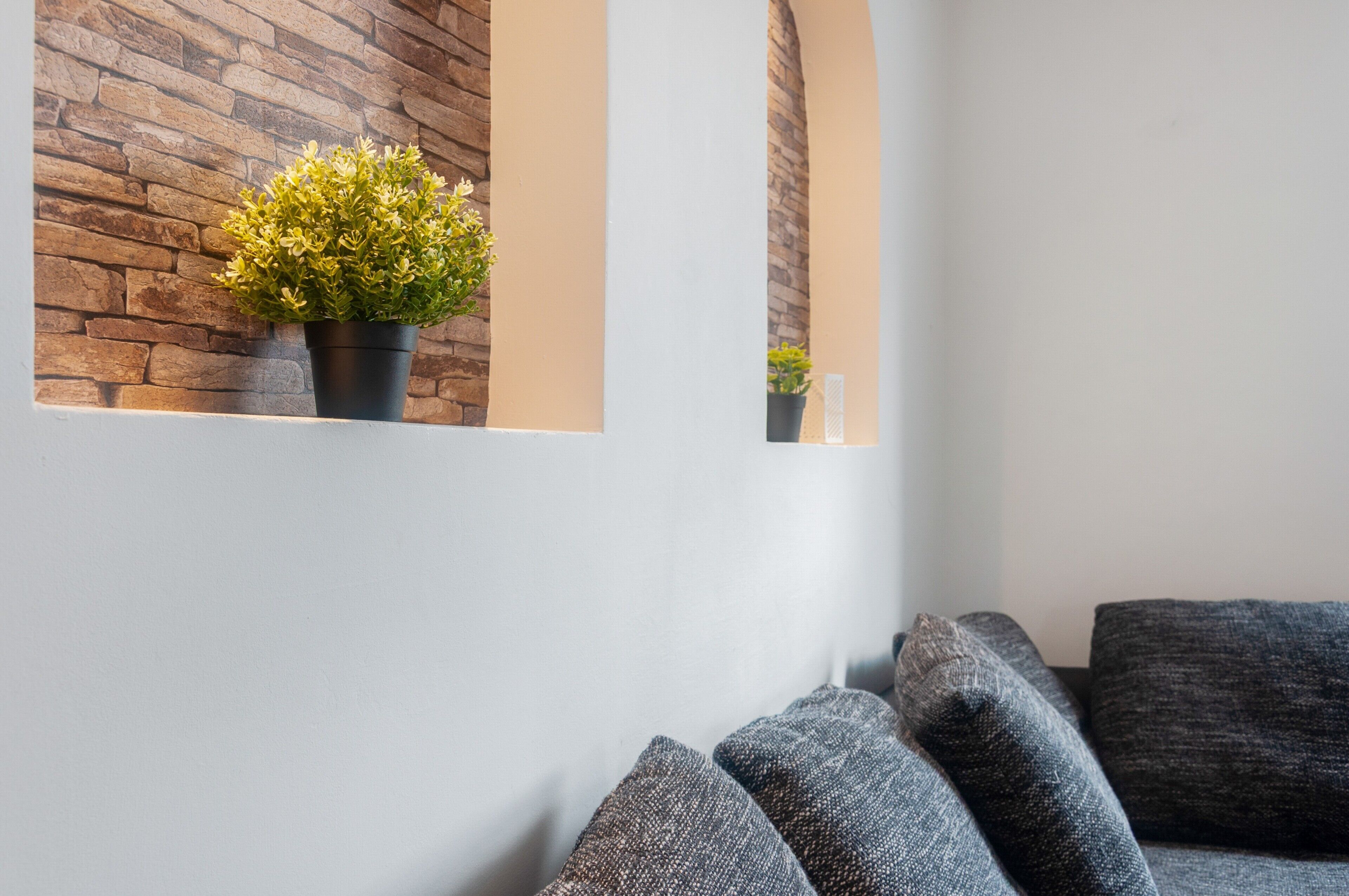 Ein modernes Interieur mit einer Steinwand, einer Topfpflanze und grauen Polstermöbeln.