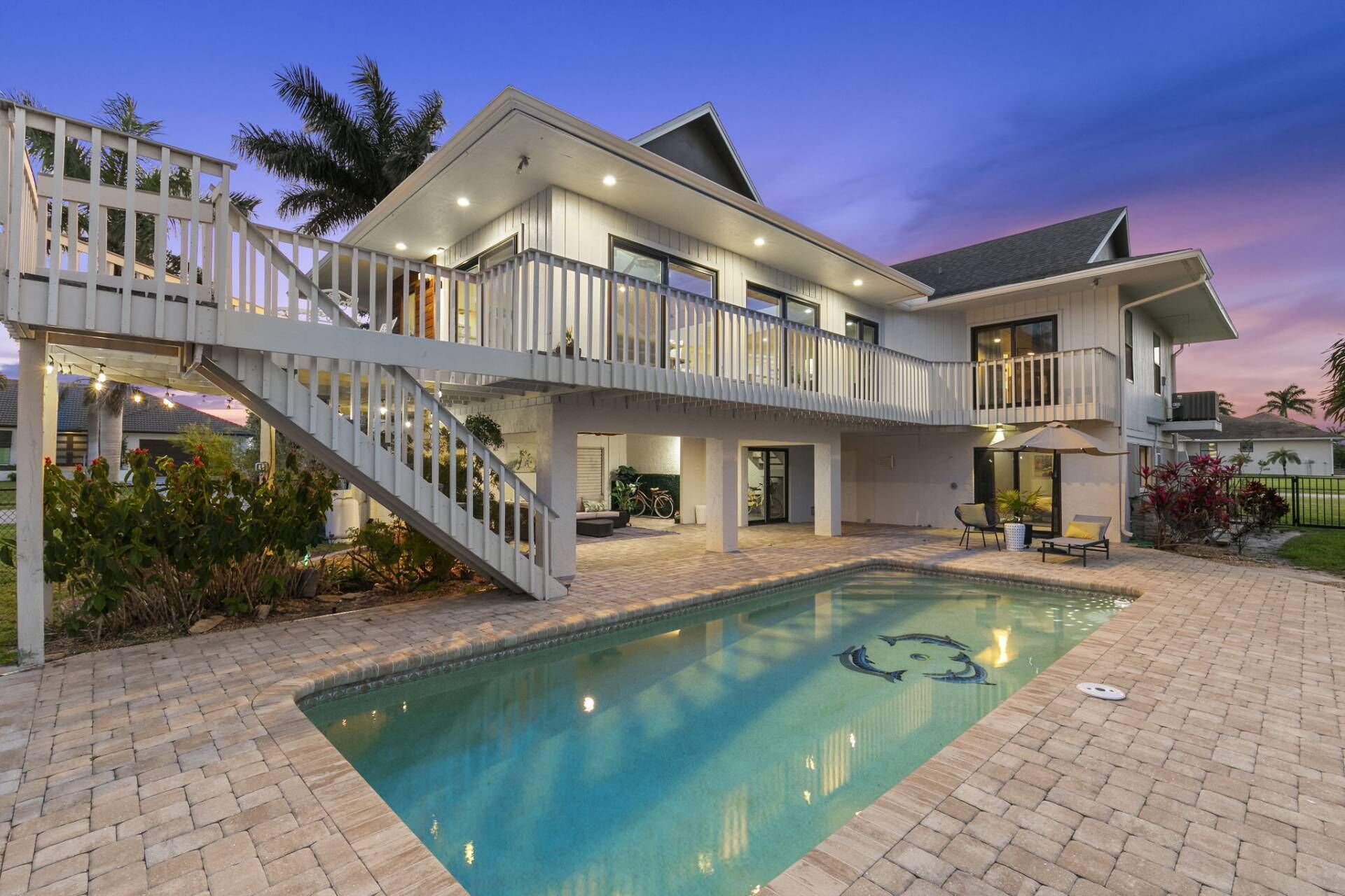 A two-story house with a swimming pool, outdoor seating, and a staircase leading to a balcony.
