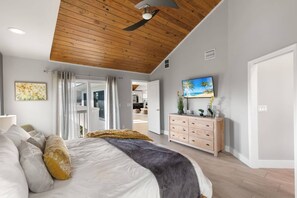 A bedroom with a bed, a ceiling fan, a TV, and a view of the kitchen. - Island Living, Perfected — Southern Island Retreat w/Pool and Dock; Close to Beach & Hotspots. (Marco Island)