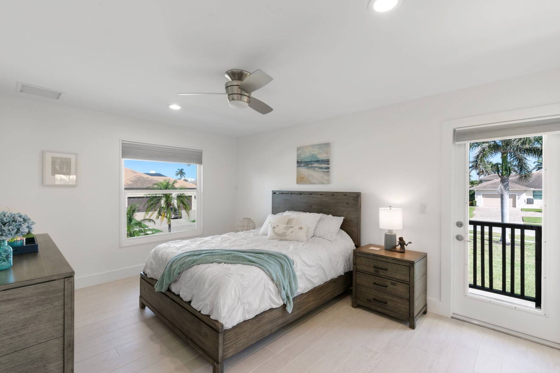 Un dormitorio con cama, mesitas de noche, ventilador de techo, ventana con vistas y puerta que da al exterior.