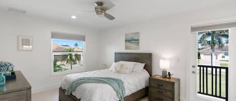 Un dormitorio con cama, mesitas de noche, ventilador de techo, ventana con vistas y puerta que da al exterior.