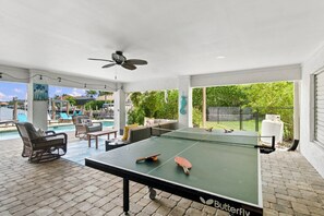 A Butterfly brand ping pong table in a covered outdoor area with a pool, seating, and a ceiling fan. - Island Living, Perfected — Southern Island Retreat w/Pool and Dock; Close to Beach & Hotspots. (Marco Island)