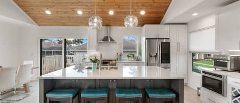 A modern kitchen with a large island, stainless steel appliances, and a wooden ceiling.