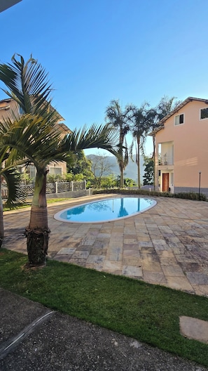A swimming pool surrounded by stone tiles, palm trees, and a building with a balcony.