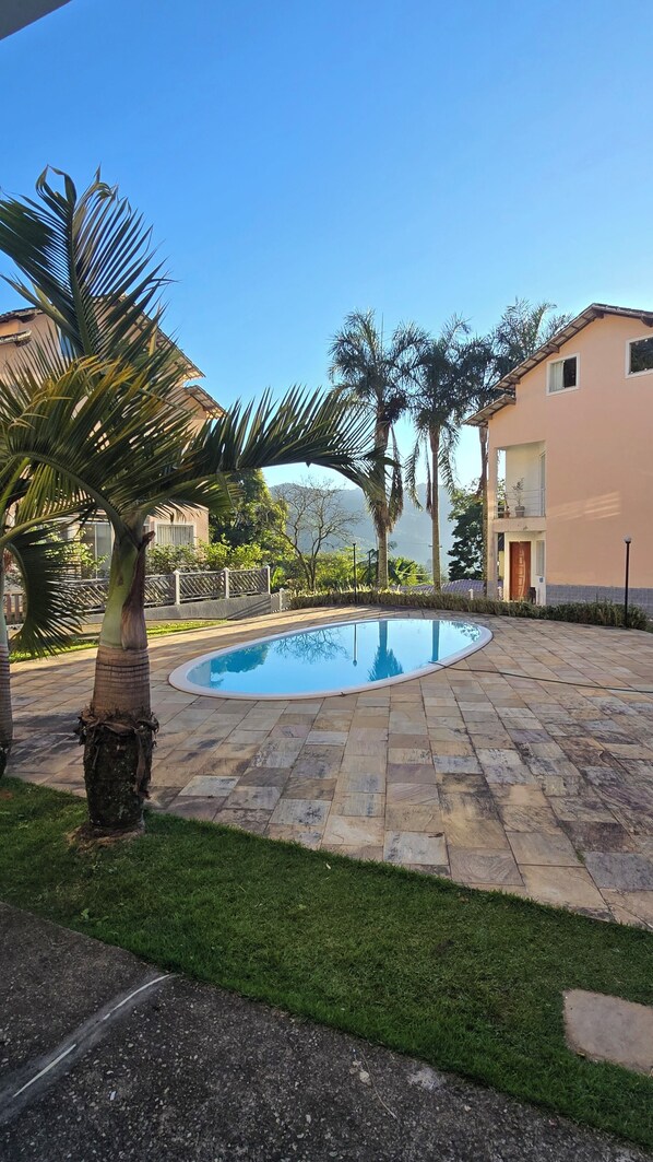 A swimming pool surrounded by stone tiles, palm trees, and a building with a balcony.