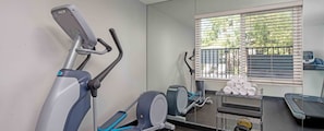 Ett gym med motionscyklar, ett löpband och ett ställ med handdukar.