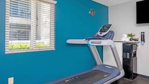 A room with a treadmill, a water dispenser, and a TV mounted on the wall.
