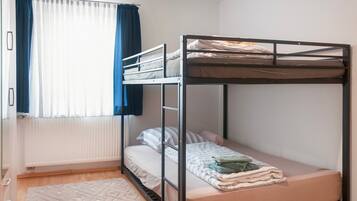 A bunk bed room with a window, curtains, and a patterned rug.