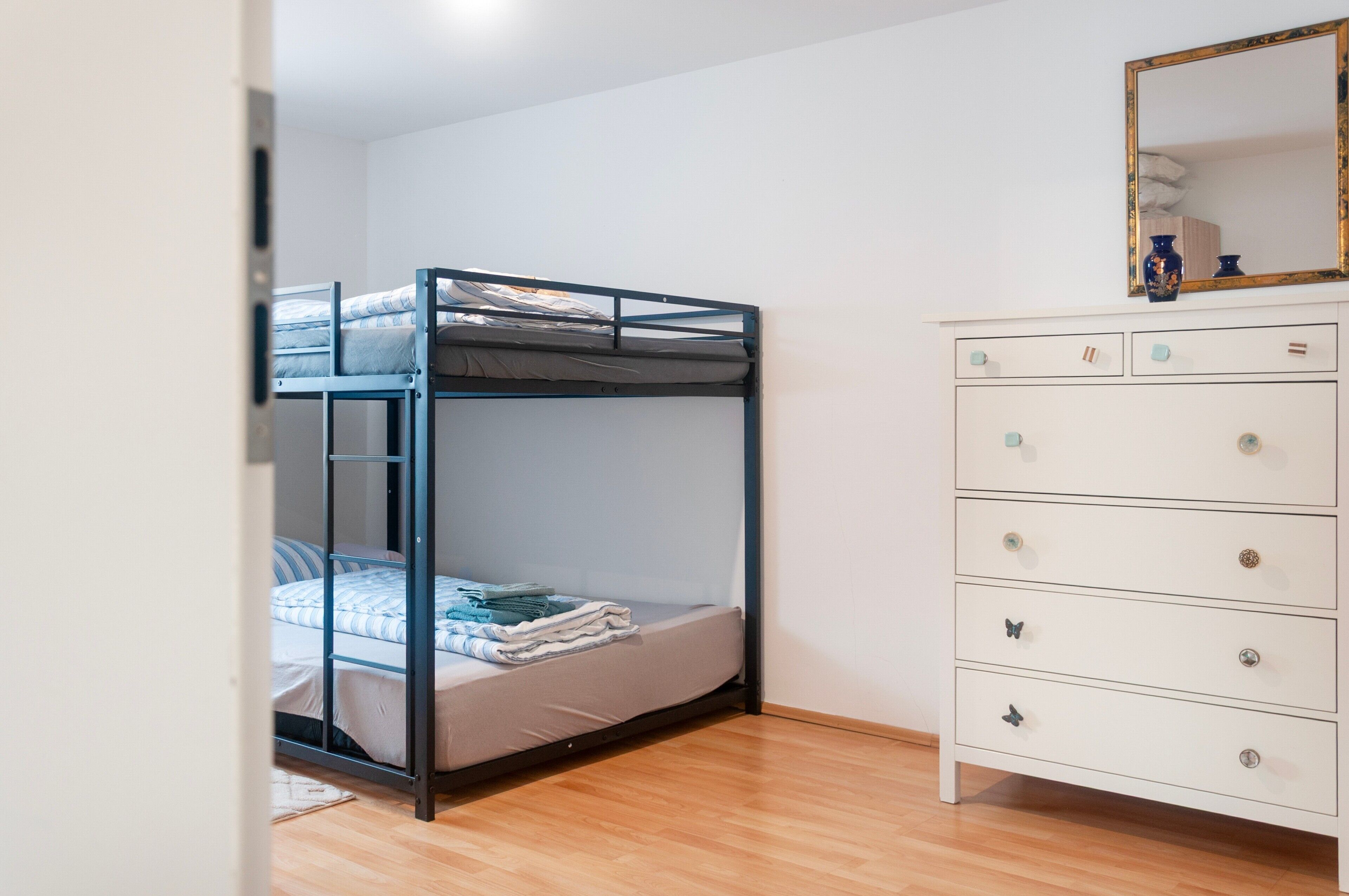 A bedroom with a bunk bed, a dresser with drawers, and a mirror on the wall.