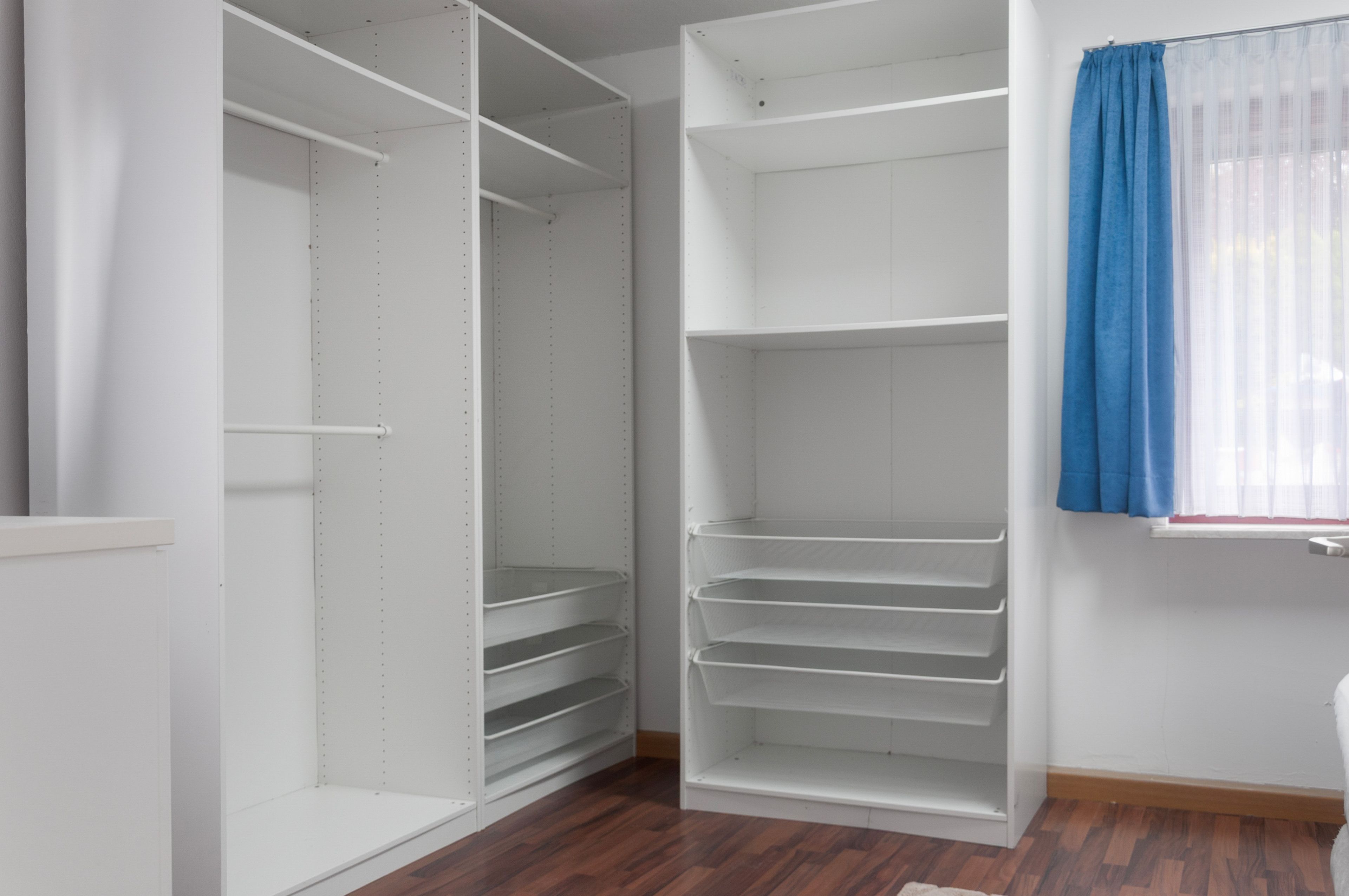 A walk-in closet with open shelving and a window with blue curtains.