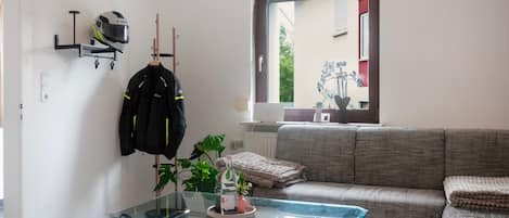 A living room with a glass coffee table, a sofa, a plant, and a helmet hanging on the wall.
