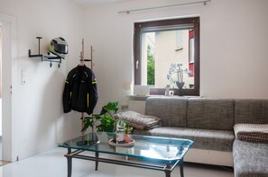 A living room with a glass coffee table, a sofa, a plant, and a helmet hanging on the wall.