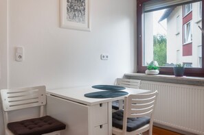 Habitació petita i blanca amb una taula, dues cadires, un radiador i una finestra que donava a edificis.