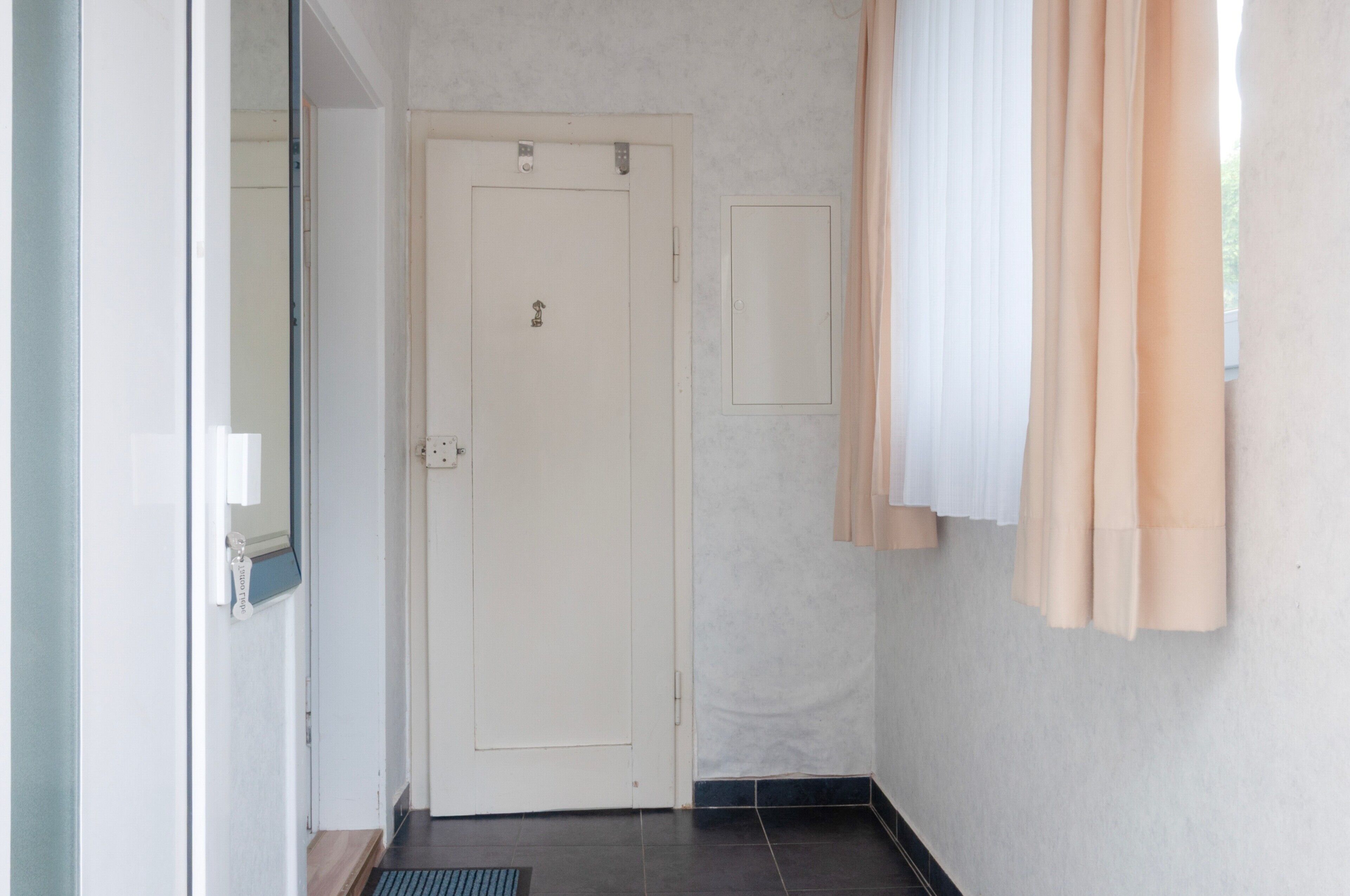 Ein Flur mit geschlossener Tür, einem kleinen Fenster mit Blick und einem Klingel.