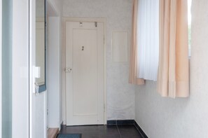 A hallway with a closed door, a small window with a view, and a doorbell.
