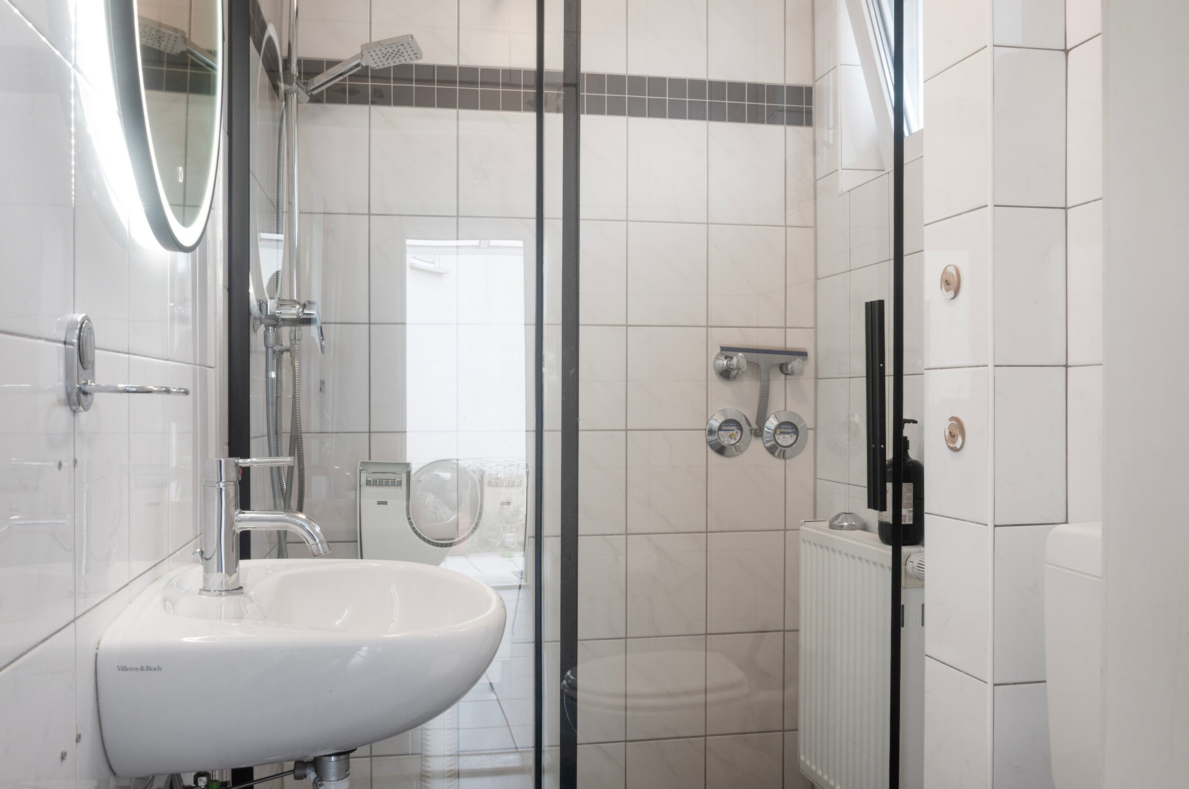 Ein modernes Badezimmer mit Duschkabine aus Glas, einem weißen Waschbecken und einer sichtbaren Toilette.