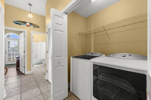 Une buanderie équipée d’un lave-linge et d’un sèche-linge, une porte donnant accès à une salle de bain et un ventilateur de plafond.