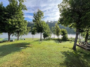 A grassy area with picnic tables and chairs, surrounded by trees and a body of water. - White River Riverside Trout Getaway, 3BR, Sleeps 8, Riverside Pavillion (Norfork)