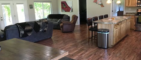 Un vaste espace de vie comprenant un coin repas avec une table en bois, un canapé et une cuisine dotée de meubles en bois et d’un îlot central.