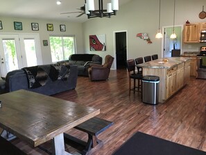 A spacious living area with a wooden dining table, a sofa, and a kitchen with wooden cabinets and a central island. - White River Riverside Trout Getaway, 3BR, Sleeps 8, Riverside Pavillion (Norfork)