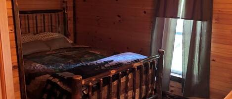Une chambre dans une cabane en bois, avec un lit, une fenêtre avec des rideaux et une porte.