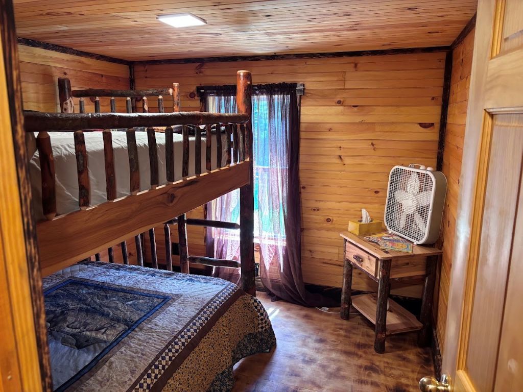 A wooden cabin room with bunk beds, a fan, and a small desk.