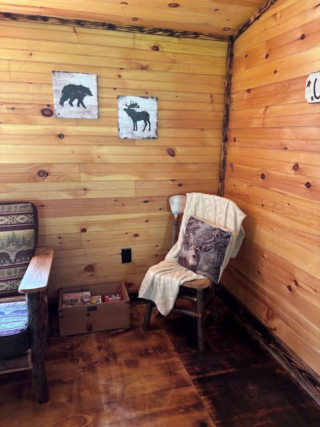 A wooden cabin interior with a wooden chair, a small table, and two animal silhouette decorations on the wall.