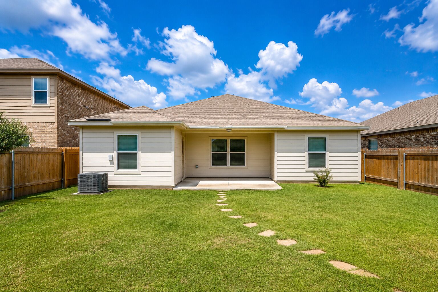 Une maison à deux étages avec un jardin devant, une clôture en bois et un ciel bleu dégagé.