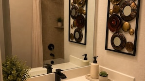 Et badeværelse med en hvid vask, sort armatur, et spejl og dekorativ vægkunst.