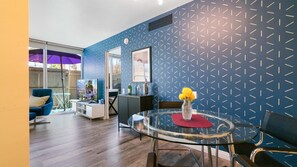 Ein modernes Wohnzimmer mit blauer Wand mit Muster, einem Glastisch mit einer Vase voller gelber Blumen und einem blauen Sessel.