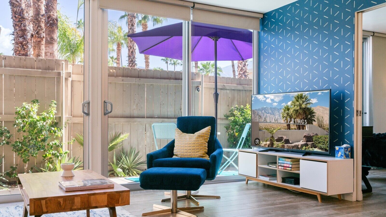 A living room with a blue armchair, a flat-screen TV, and a wooden coffee table.