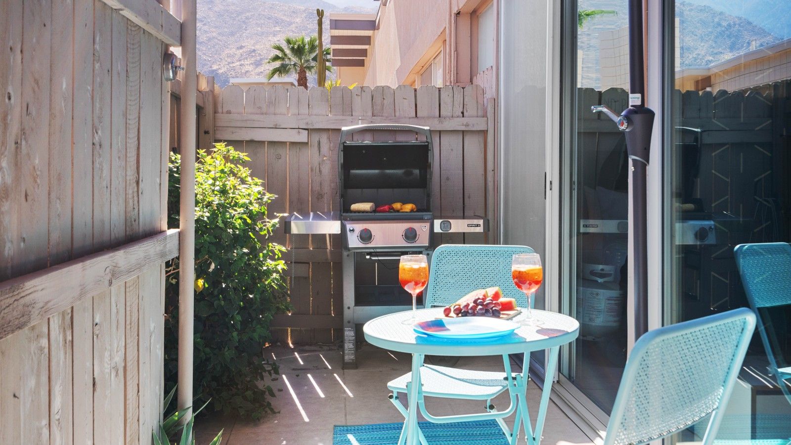 A patio with a barbecue grill, a table with chairs, and a glass door leading to a covered area.