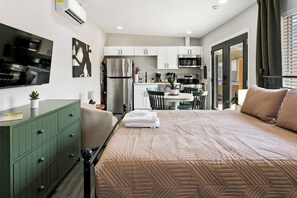 Ein modernes Schlafzimmer mit einem großen Bett, einer grünen Kommode und einem an der Wand befestigten Flachbildfernseher.