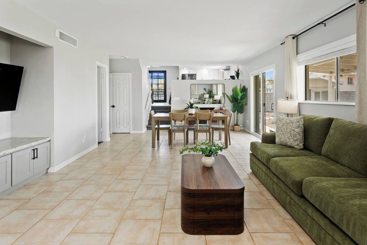 A modern living room with a flat-screen TV, a green sofa, a wooden coffee table, and a dining area with a table and chairs.