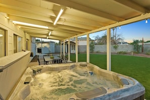 Ein überdachter Patio-Bereich mit Whirlpool, Sitzgelegenheiten im Freien und Blick auf den Garten.