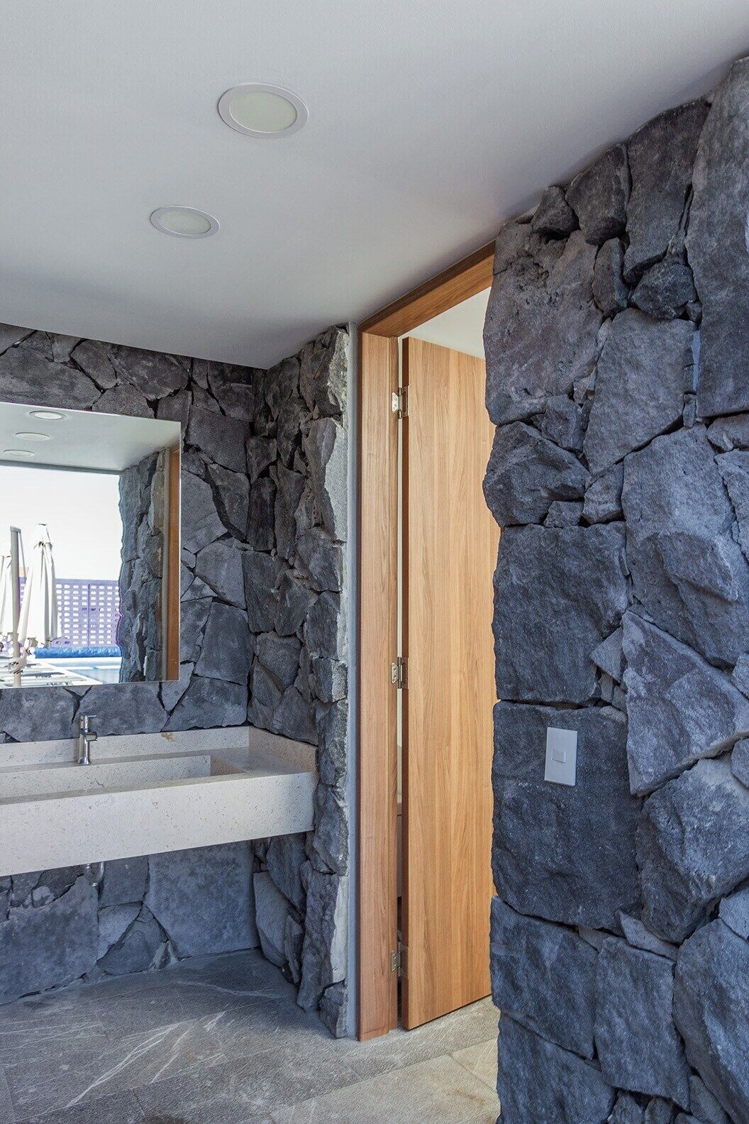 Une salle de bain avec un mur en pierre, une porte en bois et un miroir.