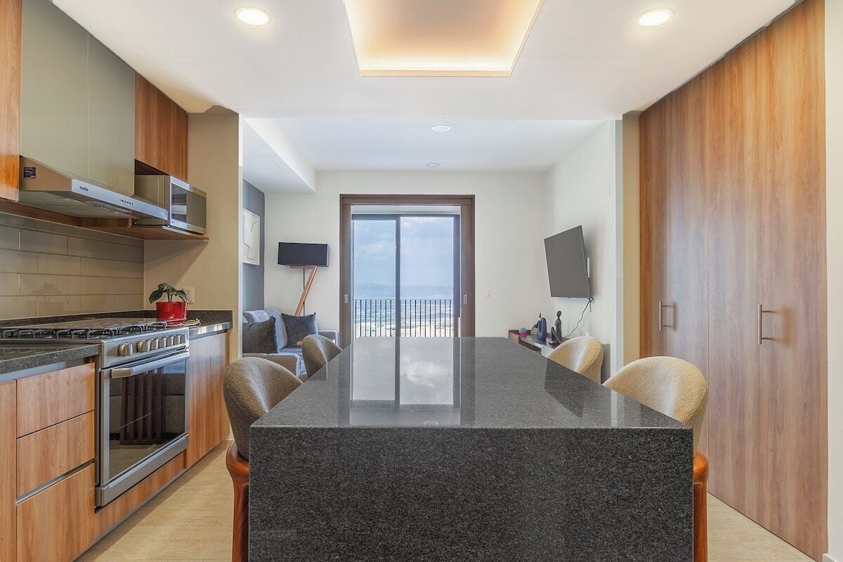 A modern kitchen with a central island, built-in oven, and a dining area with chairs.