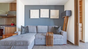 Un salon moderne avec un canapé d’angle gris, une table d’appoint en bois et un lampadaire.