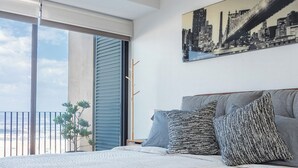 Une chambre avec un grand lit, un tableau représentant un paysage urbain et une vue sur un immeuble par une porte coulissante.