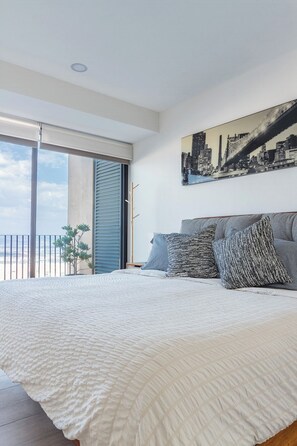 Een slaapkamer met een groot bed, een stadsgezicht schilderij en uitzicht op een gebouw door een schuifdeur.