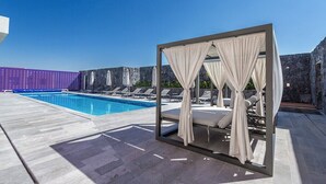 Un espace aménagé au bord de la piscine, avec un pavillon fermé par des parois de verre, des chaises longues et un ciel d’un bleu limpide.